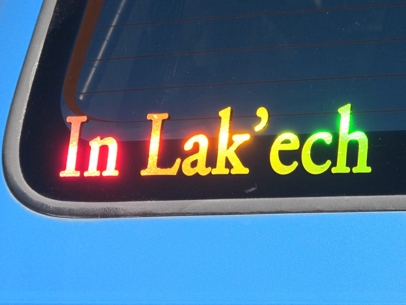 May include: A rear window sticker with the words "In Lak'ech" in rainbow colors. The sticker is on a blue car.