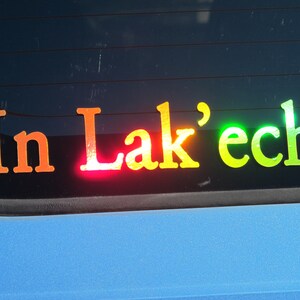 May include: A rainbow-colored sticker on a car window that reads "In Lak'ech".