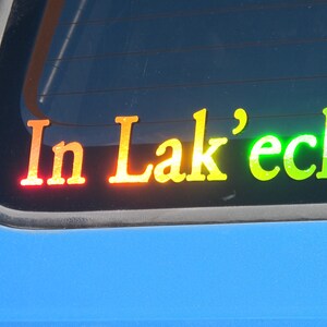 May include: A rear window sticker with the text "In Lak'ech" in rainbow colors. The sticker is on a blue car.