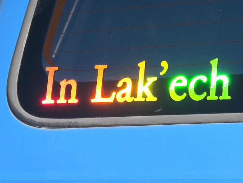 May include: A rear window sticker with the text "In Lak'ech" in rainbow colors. The sticker is on a blue car.
