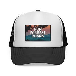Puede incluir: Gorra de camionero en blanco y negro con visera curva. El panel frontal blanco presenta un parche rectangular con el texto "RUN FORREST RUNNN" sobre un paisaje de montañas y árboles.