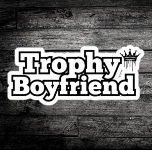 May include: Black and white graphic design with the text "Trophy Boyfriend" and a crown above the word "Trophy".