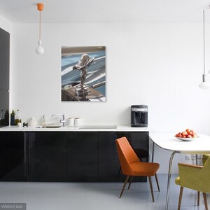 May include: A framed print of a silver Rolls-Royce hood ornament, the Spirit of Ecstasy, displayed in a modern kitchen. The kitchen features black cabinets, a white countertop, and a dining table with colourful chairs.