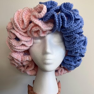 May include: A crocheted hat with pink and blue ruffles. The hat is on a white mannequin head.