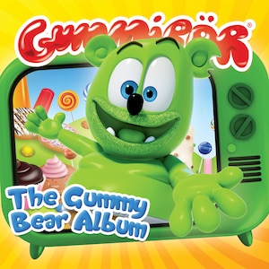 May include: A green gummy bear cartoon character with large eyes and a wide smile is peeking out of a green television screen. The screen shows a colourful candy land scene. The text "The Gummy Bear Album" is written below the screen.