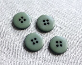 May include: Four olive green buttons with four holes each, arranged on a light gray textured fabric. The buttons are round and have a matte finish. Ideal for sewing projects or adding a decorative touch to garments.