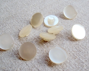 May include: A collection of ten white oval and round buttons. The buttons are made of a smooth, shiny material and have a slight iridescent sheen.