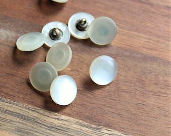 May include: A collection of nine white iridescent buttons with a shiny finish. The buttons are round and have a flat back.