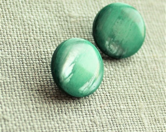 May include: Two round, green earrings with a marbled white pattern. The earrings are set against a textured, light gray fabric background. The earrings have a glossy finish and a smooth surface.