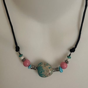 May include: A turquoise, pink, and white beaded necklace with a large, mottled turquoise stone pendant. The necklace is on a black cord.
