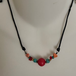 May include: A red, orange, and turquoise beaded necklace with a large red bead in the center. The necklace is on a black cord.