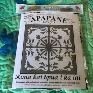 Puede incluir: Un patrón de edredón de Apapane Designs, con un diseño central de rayos de sol con tortugas y delfines. El patrón mide 107 cm x 107 cm e incluye instrucciones. El paquete está sobre un fondo acolchado con tonos azules y verdes.