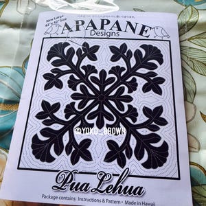 May include: A white paper pattern for a quilt titled APAPANE Designs Pua Lehua. The pattern features a large black floral motif with dashed stitching lines, text reading New Large 42"x 42" Size, @YOKO_BROWN, and Package contains: Instructions & Pattern • Made in Hawaii.