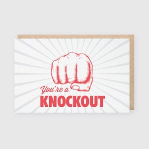 May include: A greeting card with a red illustration of a fist and the text "You're a Knockout" in red.