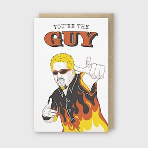 May include: A greeting card featuring a cartoon illustration of a man with blonde hair and a goatee wearing a black and orange shirt with flames. The text "YOU'RE THE GUY" is printed in red and orange letters.