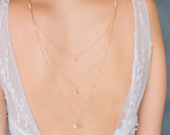 May include: A delicate gold back necklace with three strands of chain and three pearl pendants.