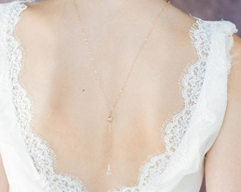 May include: A delicate gold chain necklace with a small crystal pendant. The necklace is worn by a person with a white lace top.