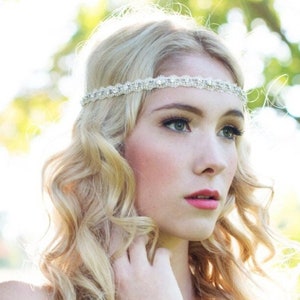 May include: A woman with long, blonde, curly hair wearing a silver headband with rhinestones. She is wearing light makeup and has a natural, relaxed expression.