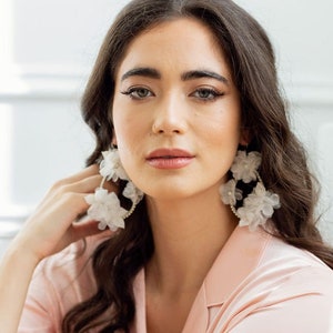 large oversized teardrop earrings with handwired crystals on teardrop frame. Handpressed silk flowers float along the teardrop.  Each flower is finished with a crystal and so are accented with clay leaves. Available in silver and Ivory