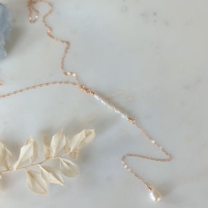 May include: A delicate gold chain necklace with a single pearl pendant and a row of smaller pearls in the center.