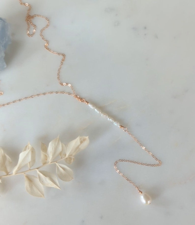 May include: A delicate gold chain necklace with a single pearl pendant and a row of smaller pearls in the center.