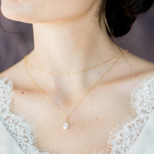 May include: A delicate gold chain necklace with a single pearl pendant. The necklace is layered with a thinner gold chain.