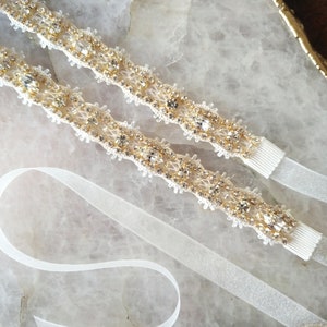 May include: Two pieces of ivory-colored beaded trim with clear rhinestones and gold accents. The trim is on a white background.