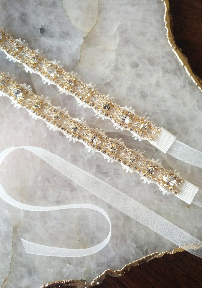 May include: Two pieces of ivory-colored beaded trim with clear rhinestones and gold accents. The trim is on a white background.