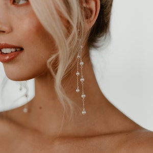 Puede incluir: Una mujer con largos pendientes de perlas. Los pendientes son de plata y tienen varias hileras de perlas.