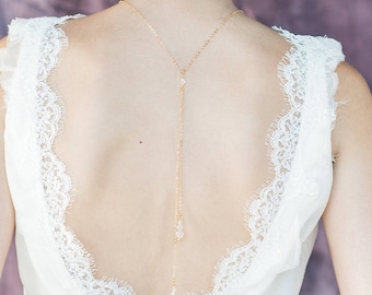 May include: A gold back necklace with a delicate chain and crystal accents. The necklace is worn by a model with a white lace top.