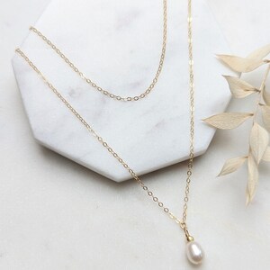 May include: A delicate gold chain necklace with a single white pearl pendant.