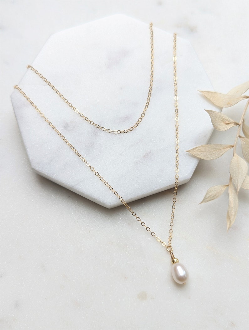 May include: A delicate gold chain necklace with a single white pearl pendant.