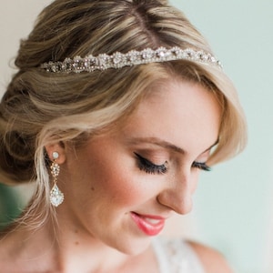 May include: A bride with blonde hair wearing a delicate silver headband with rhinestones and matching teardrop earrings with rhinestones.