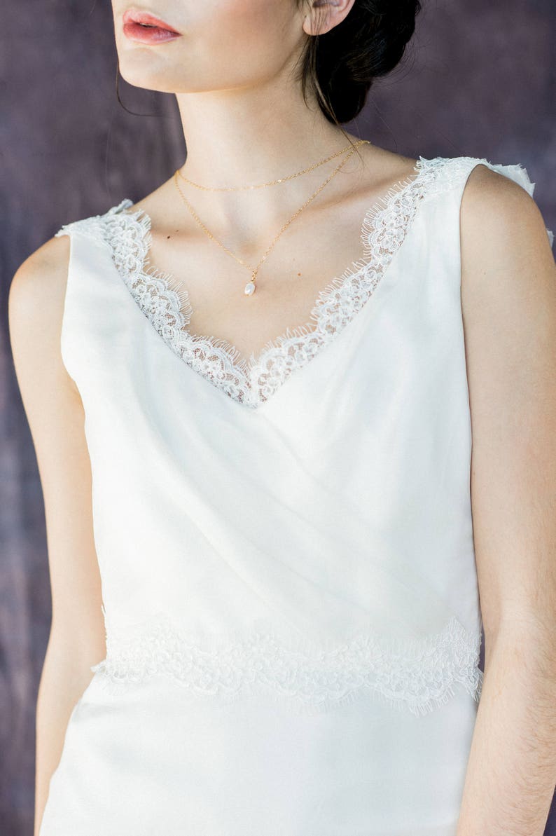 May include: A white sleeveless dress with a lace trim around the neckline and hem. The dress has a simple, elegant design and is perfect for a special occasion.