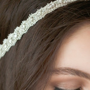 May include: A silver headband with rhinestones and a delicate design. The headband is worn on a person's head with their hair pulled back.