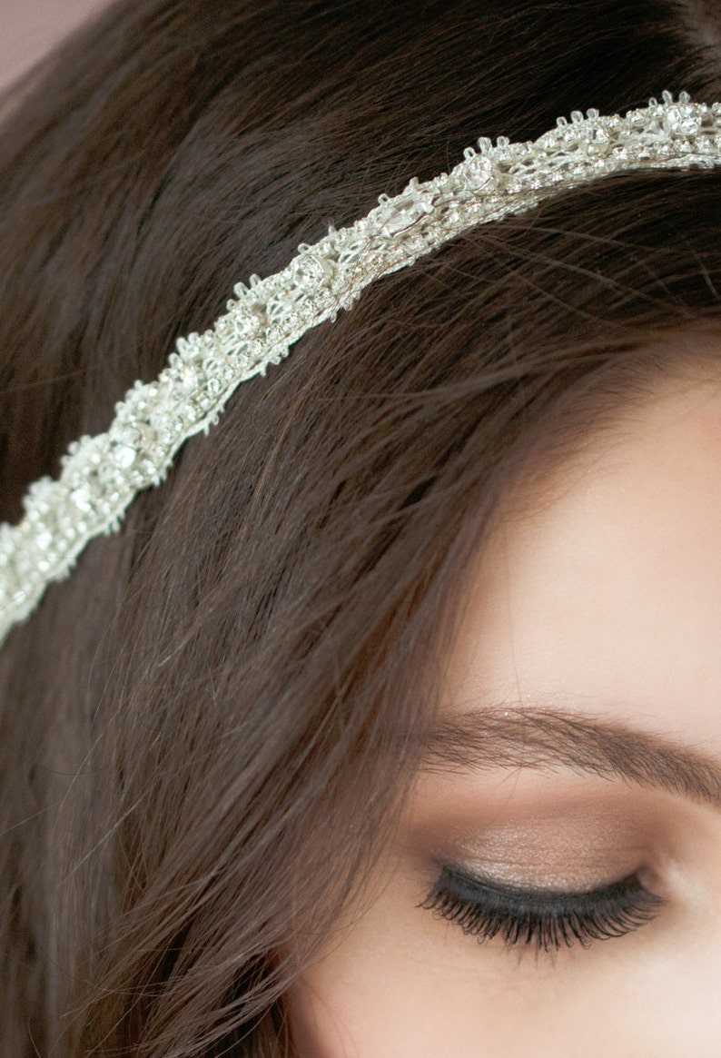 May include: A silver headband with rhinestones and a delicate design. The headband is worn on a person's head with their hair pulled back.