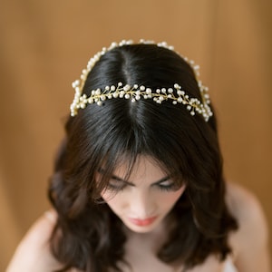 May include: A woman with dark hair wearing a gold and pearl hairpiece. The hairpiece is a delicate vine design with small pearls.