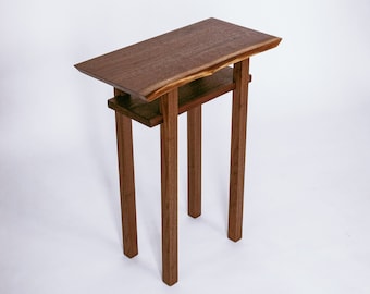 May include: A small wooden end table with a live edge top and four legs. The table has a shelf underneath the top.