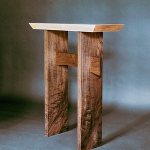 May include: A wooden table with a light wood top and dark wood legs. The legs are connected by a cross brace.