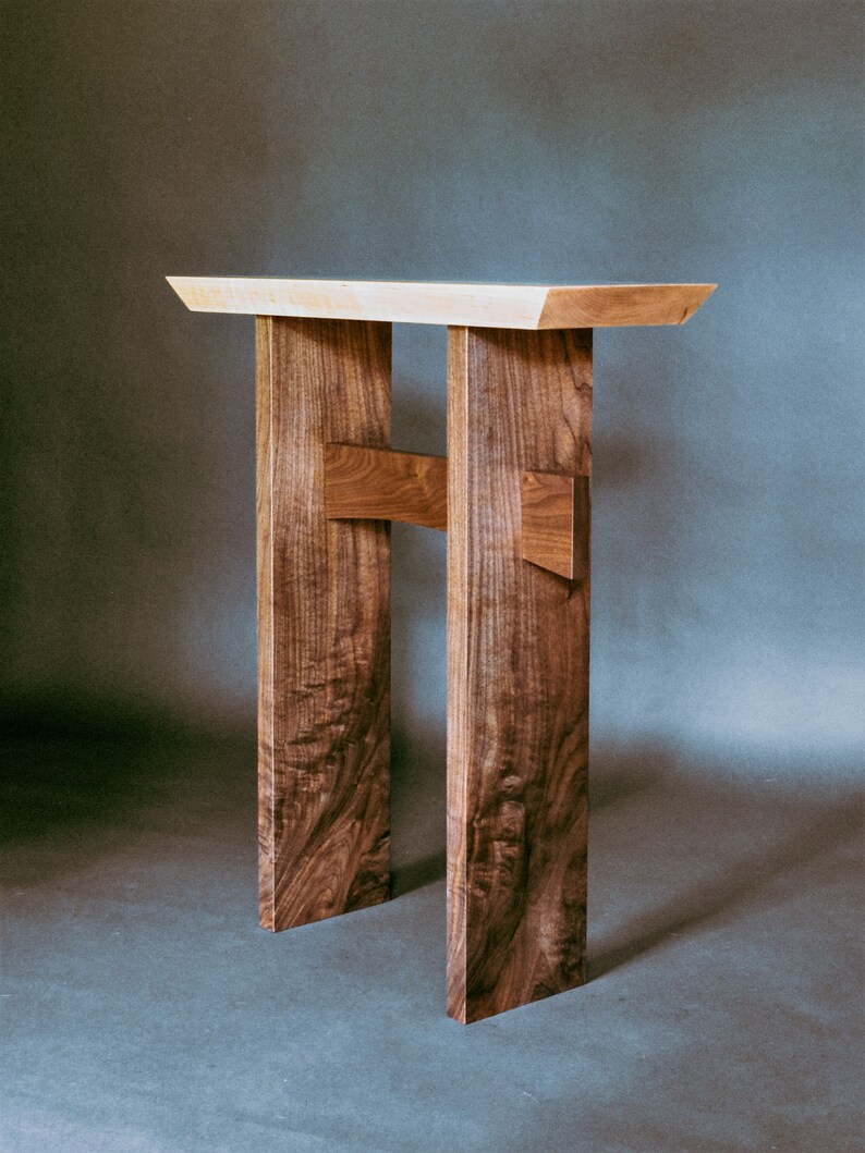 May include: A wooden table with a light wood top and dark wood legs. The legs are connected by a cross brace.