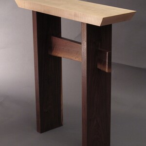 May include: A modern console table with a light wood top and dark wood legs. The table has a simple, minimalist design and would be a great addition to any home.