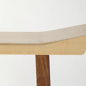 May include: A wooden bench with a light wood top and dark wood legs. The top of the bench is curved and has a slight slope.