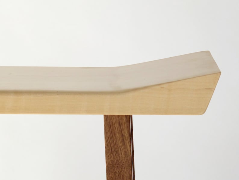 May include: A wooden bench with a light wood top and dark wood legs. The top of the bench is curved and has a slight slope.