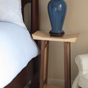 May include: A wooden end table with a light wood top and dark wood legs. A blue ceramic lamp with a white shade sits on the table.