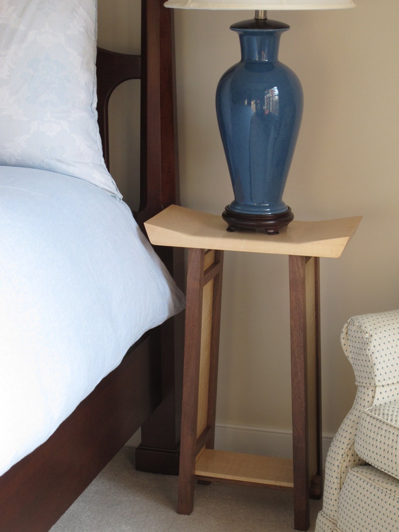 May include: A wooden end table with a light wood top and dark wood legs. A blue ceramic lamp with a white shade sits on the table.