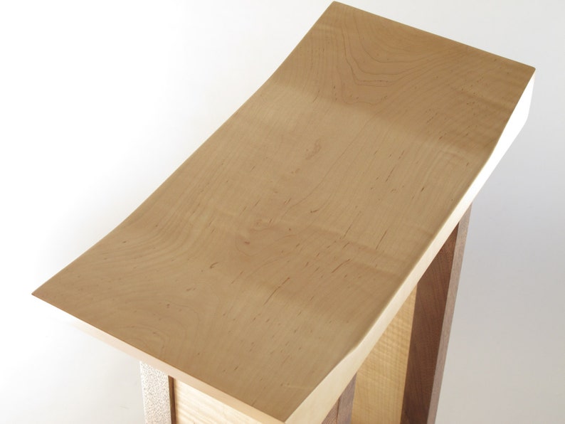 May include: A wooden stool with a curved, light brown top and a base made of darker wood.