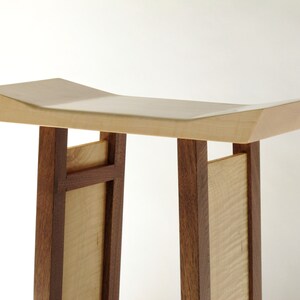 May include: A wooden stool with a light wood top and dark wood legs. The top is curved and the legs are rectangular. The stool is made of two different types of wood.