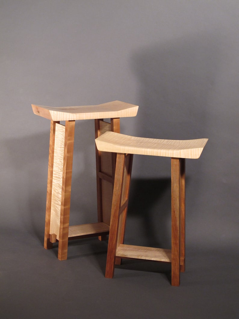 May include: Two wooden stools with a light wood top and dark wood legs. The stools are stacked on top of each other.