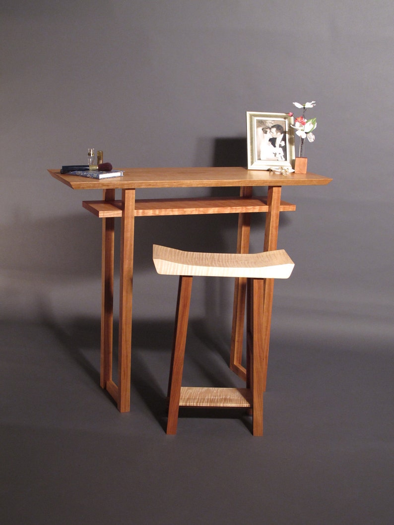 May include: A wooden table with a shelf and a matching stool. The table has a light wood finish and the stool has a natural wood finish. There is a framed photograph and a vase with flowers on the table.
