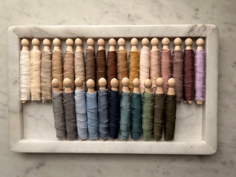 May include: A collection of 30 spools of silk ribbon in various shades of brown, blue, and pink, arranged in a wooden tray. The ribbon is wound around wooden dowels.